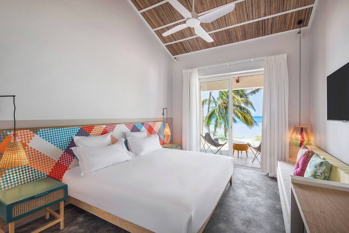Habitación de hotel con cama, escritorio, silla, ventilador de techo y vista a la playa.