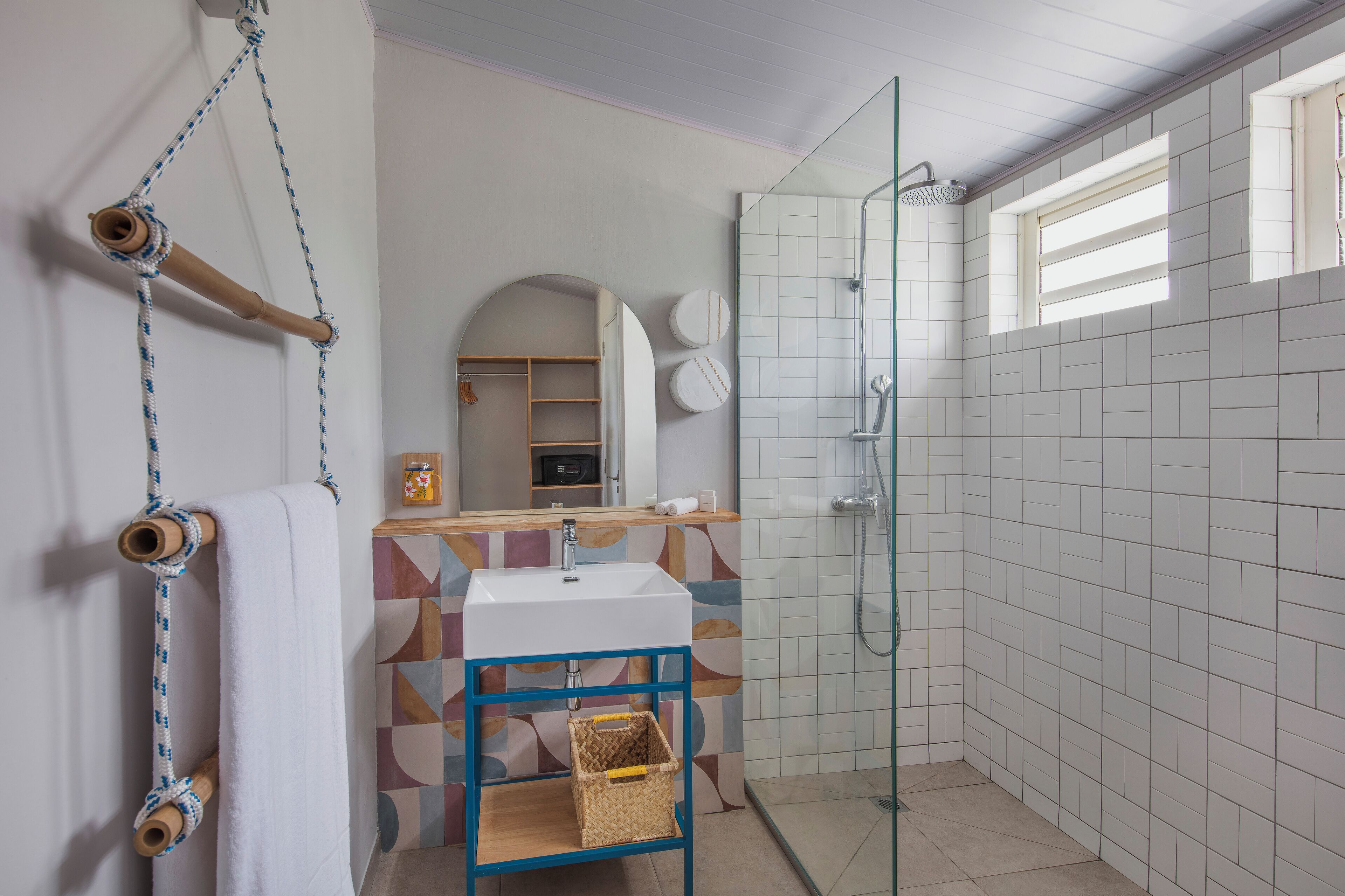Un baño con cabina de ducha de vidrio, un lavabo blanco y un perchero de madera.