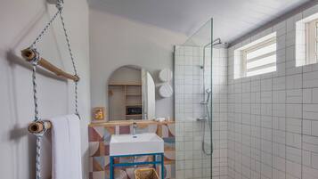 Un baño con cabina de ducha de vidrio, un lavabo blanco y un perchero de madera.