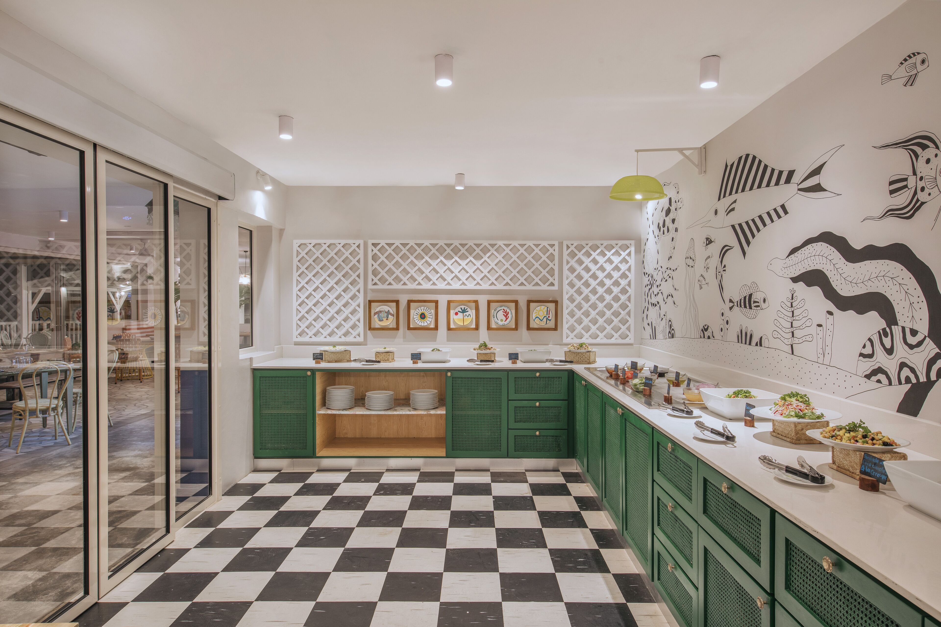 A modern kitchen with green cabinets, a checkered floor, and a wall decorated with fish illustrations.