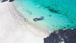 Vista aérea de una playa con aguas turquesas transparentes, un bote anclado cerca de la orilla y afloramientos rocosos.