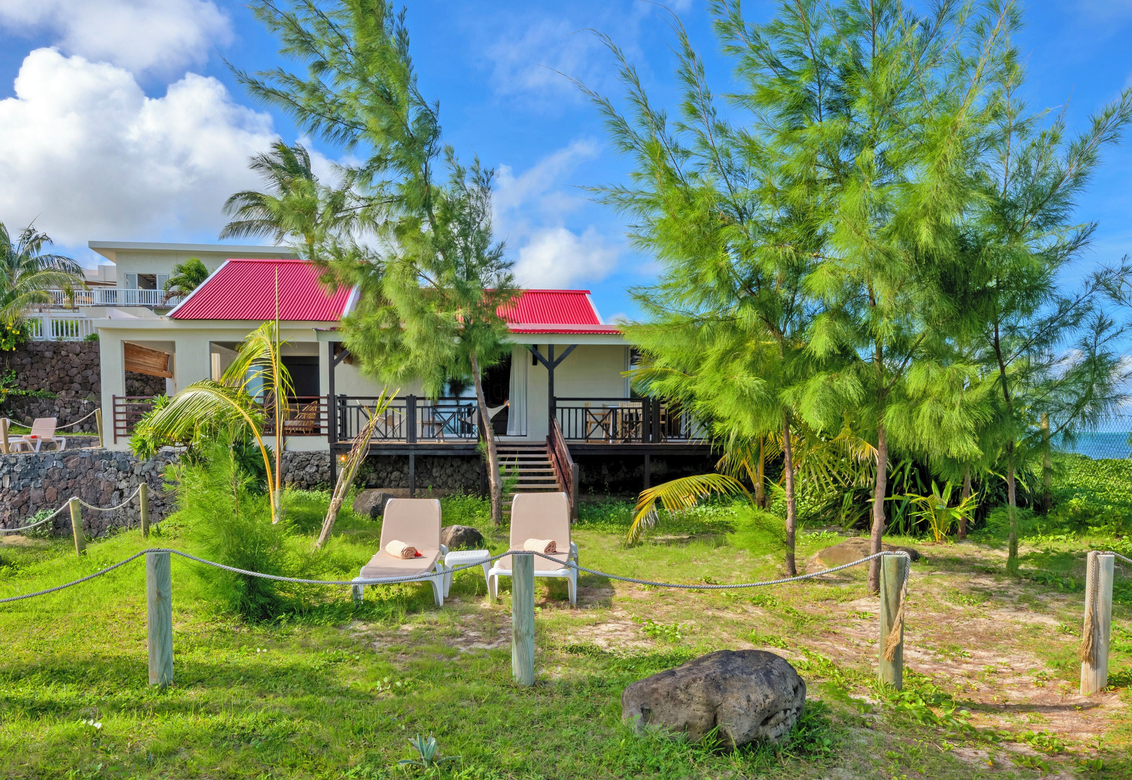 A resort with a red-roofed building, two lounge chairs, and a stone wall.