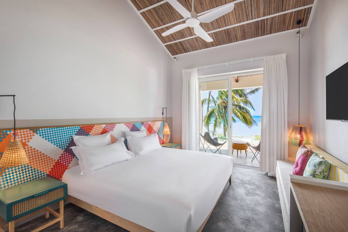 Habitación de hotel con cama, escritorio, silla, ventilador de techo y vista a la playa.