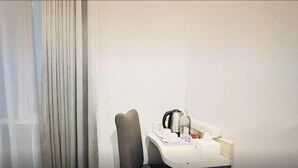 A hotel room with a bedside table, a chair, and a small tray with a kettle and cups. - VIO Westhoff (Bandung)