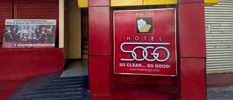 L’entrée d’un hôtel avec une façade rouge et jaune, une enseigne indiquant « HÔTEL 500 » et un slogan : « TELLEMENT PROPRE… TELLEMENT BIEN ! »