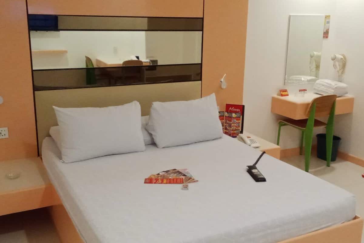 A hotel room with a bed, a desk, a chair, a mirror, and a telephone.