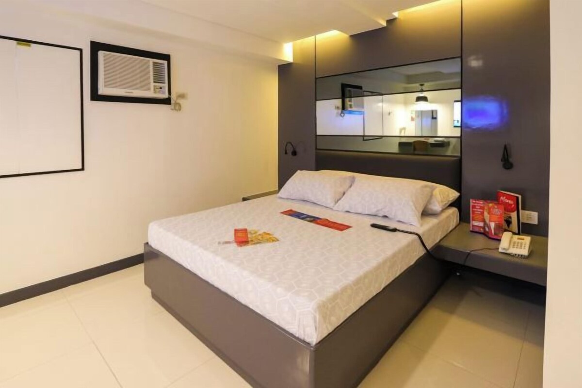 A modern hotel room with a large bed, a bedside table with a phone, a mirror, and a wall-mounted air conditioner.