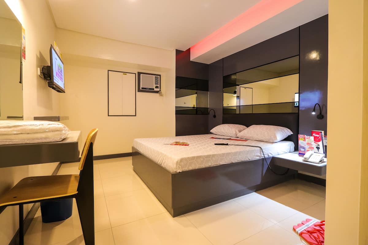 A modern hotel room with a bed, bedside table, chair, and a TV mounted on the wall.