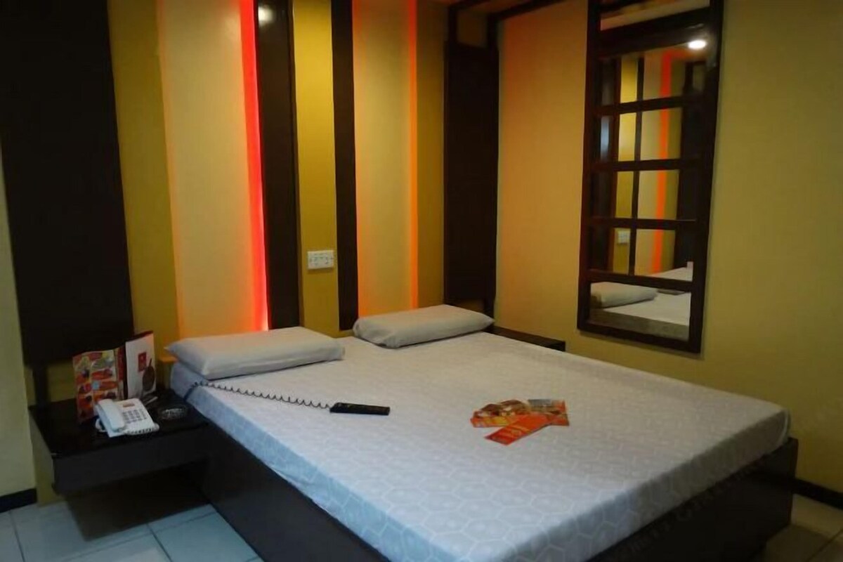A hotel room with a bed, a nightstand with a phone, a remote control, and a magazine.