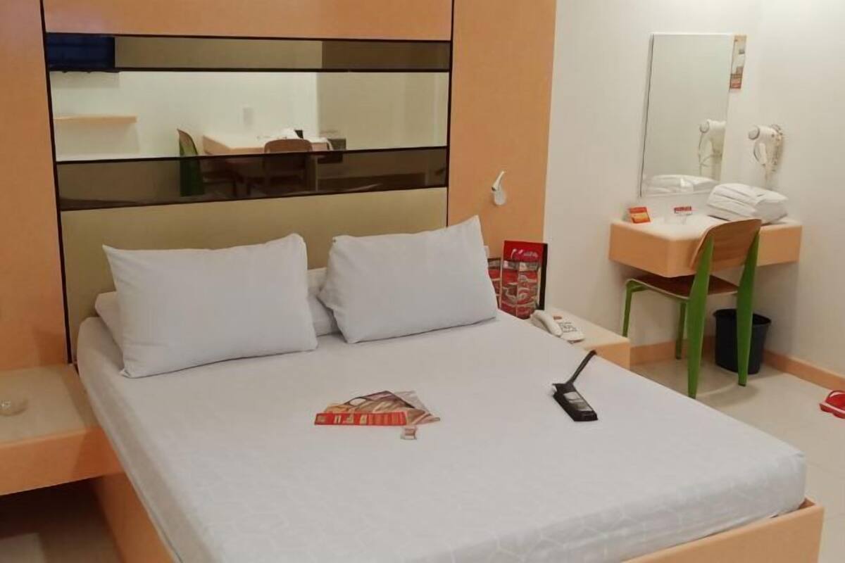 A bed with white bedding, a bedside table with a phone, a mirror above the sink, and a chair.