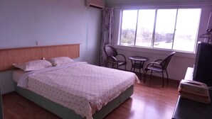 A bedroom with a bed, a window, a chair, a small table, and a TV. - Hotel Hung Hung (Kuching)