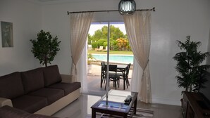 Un salón con sofá, una mesa de centro de vidrio y vista a una piscina a través de un ventanal.