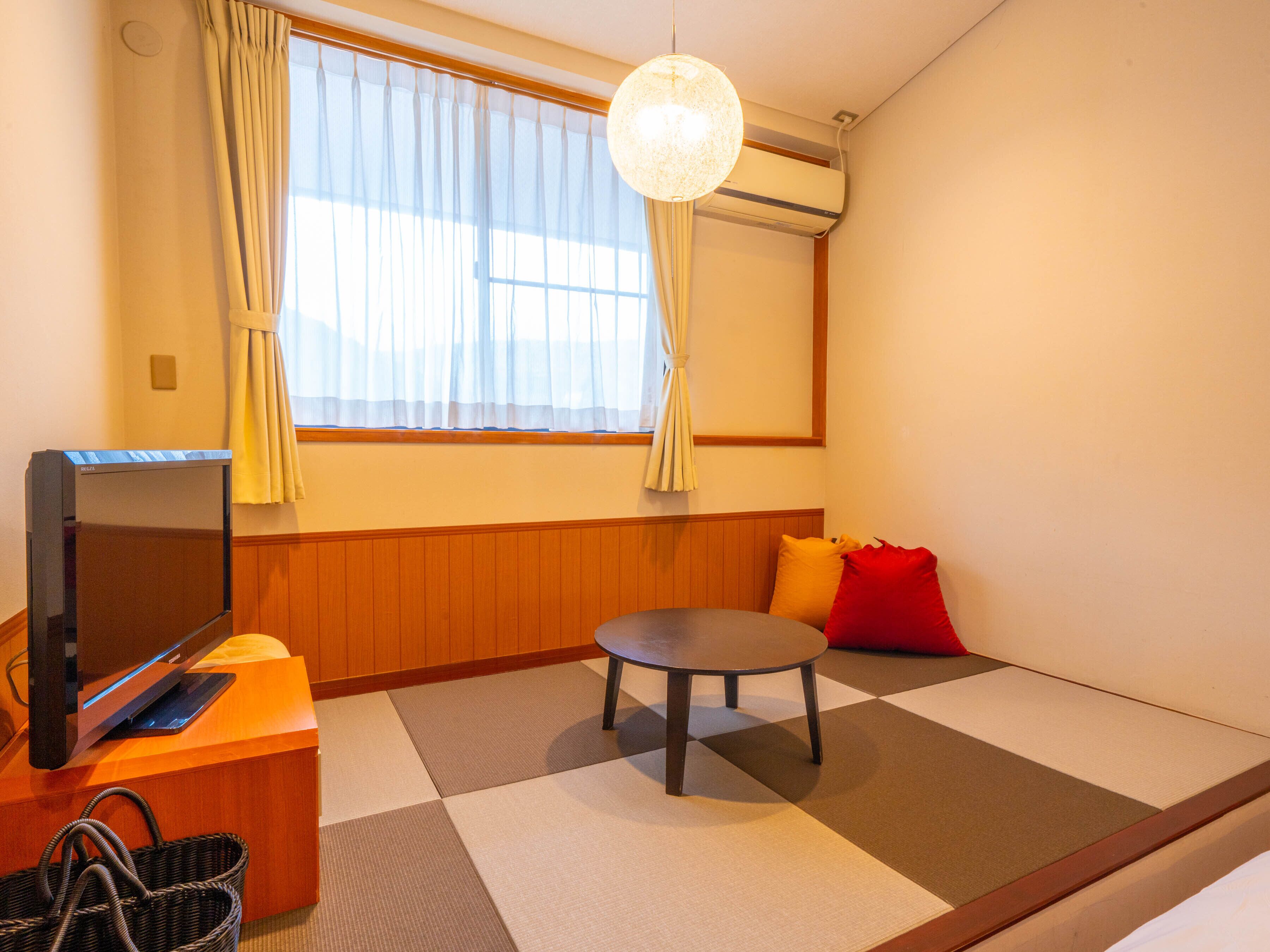 A room with tatami flooring, a television, a small table, and a red cushion.