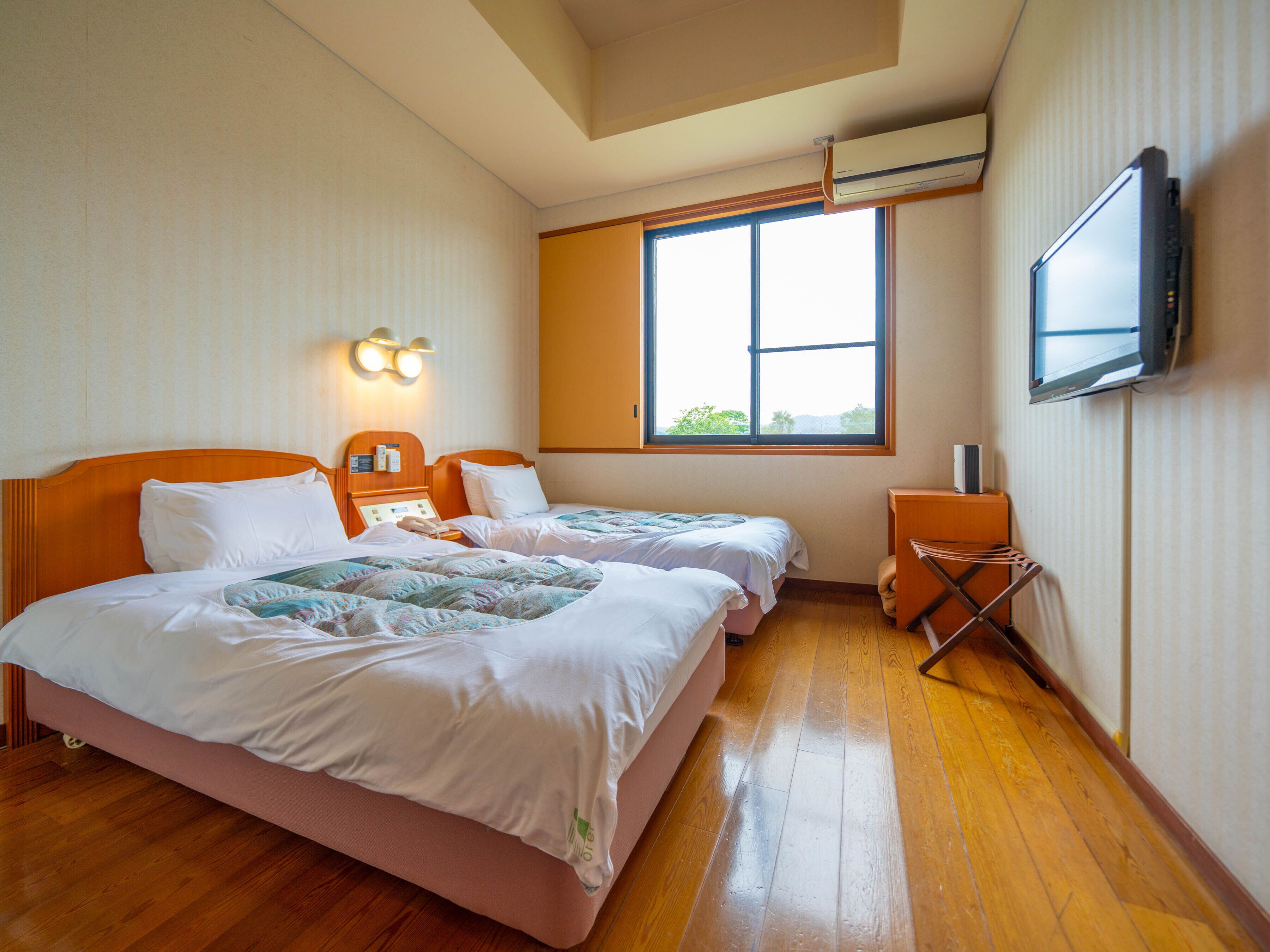 A hotel room with two beds, a TV, a desk, and a window.