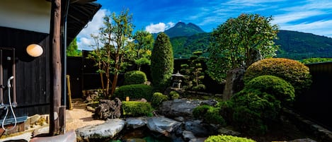 Un jardín japonés tradicional con un estanque de carpas, formaciones rocosas y una montaña al fondo.