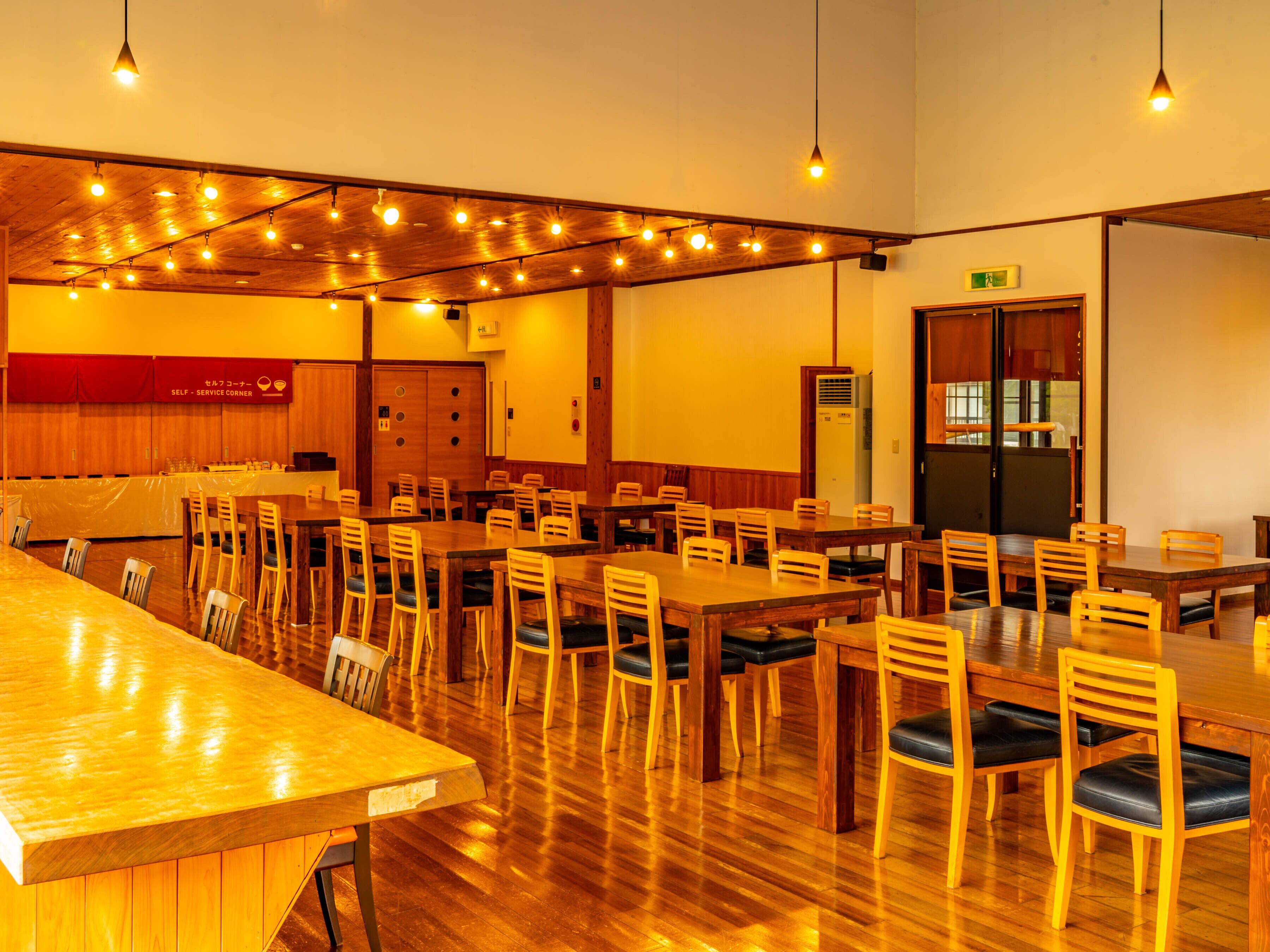 A spacious dining area with wooden tables and chairs, a service corner, and a kitchen area.