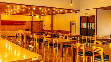 A spacious dining area with wooden tables and chairs, a service corner, and a kitchen area.