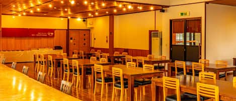 Un comedor amplio con mesas y sillas de madera, un espacio de servicio y una cocina.