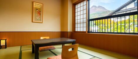 A traditional Japanese room with tatami flooring, a low table, and a view of mountains through a large window.