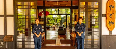 A traditional Japanese entrance with two individuals in uniform standing at the threshold.