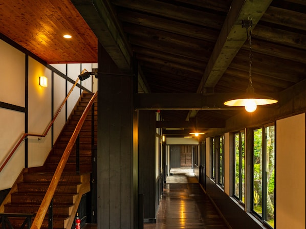A hallway with wooden floors, a staircase on the left, and large windows on the right.