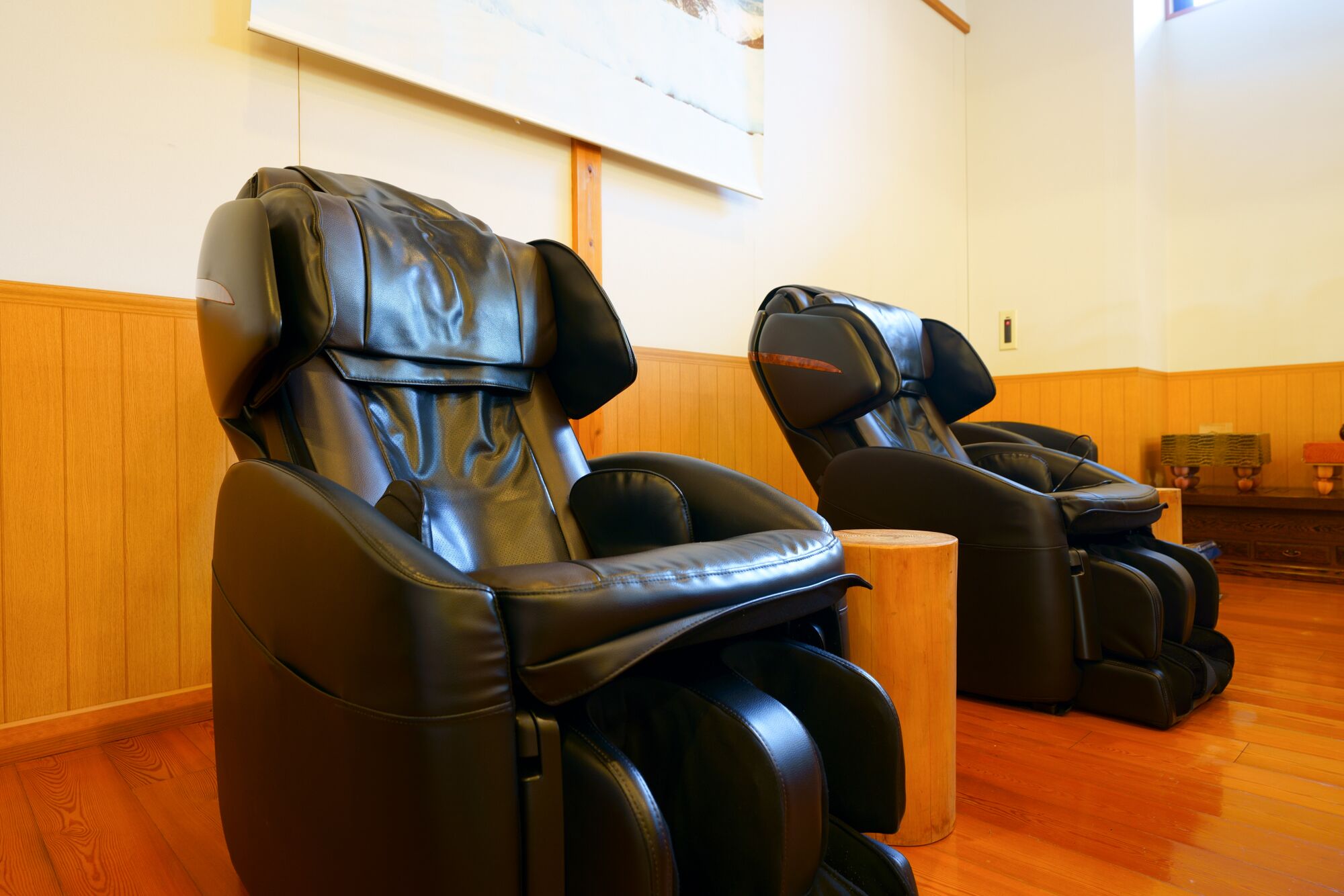 Two massage chairs in a room with wooden flooring and a wooden panel wall.