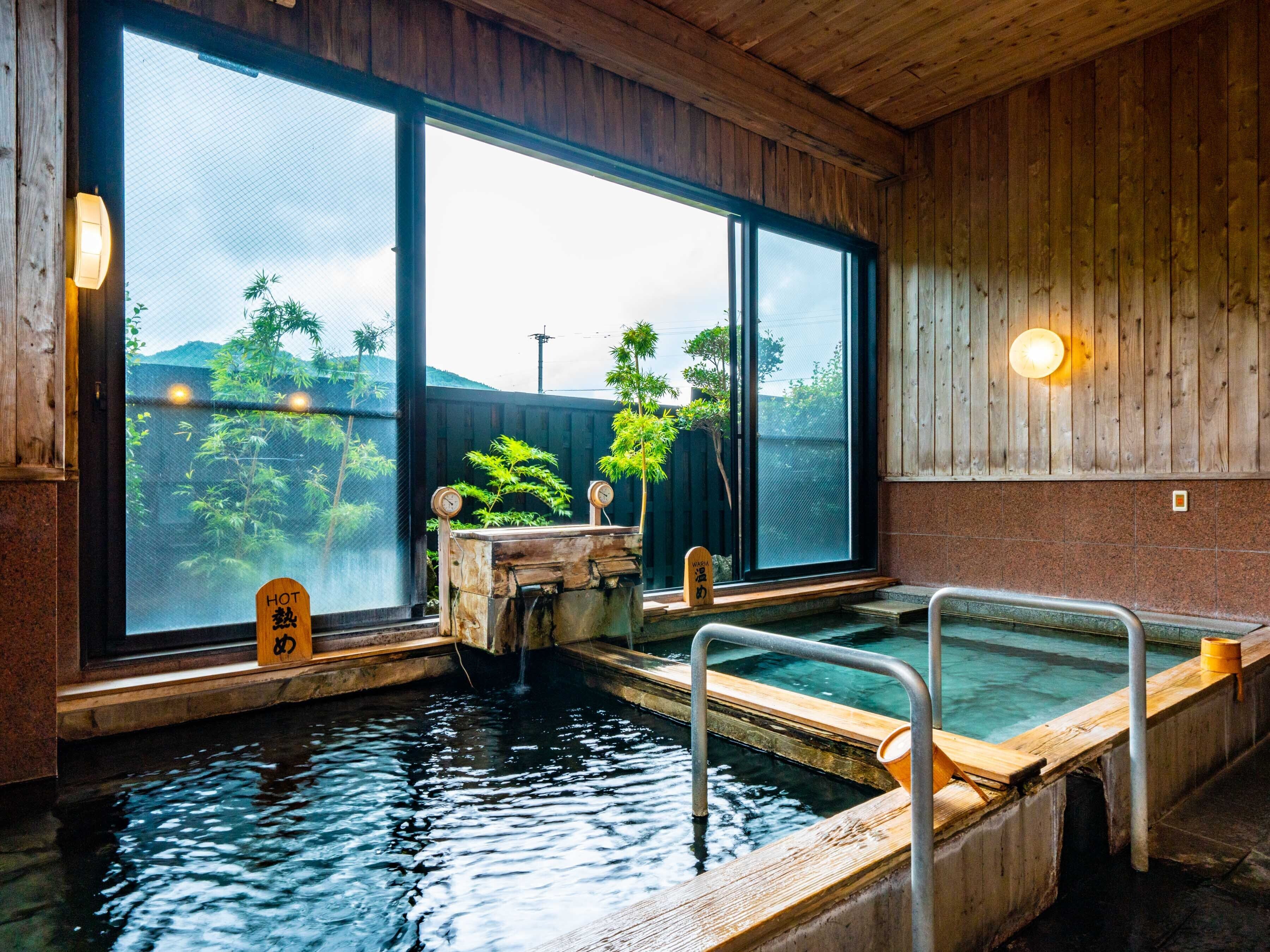 A traditional Japanese onsen with wooden interiors, a hot spring bath, and a view of greenery outside.