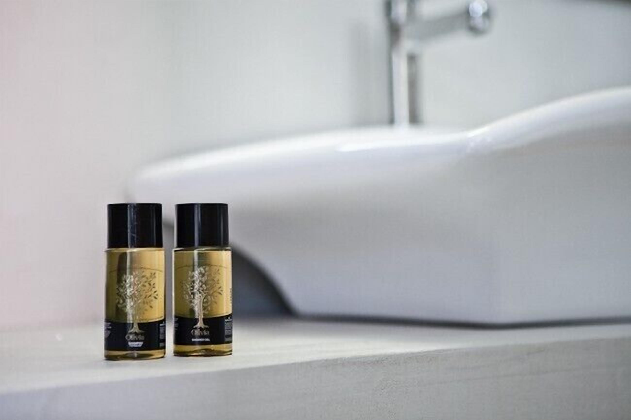 Dos botellas de perfume sobre una encimera de baño con un lavabo blanco al fondo.