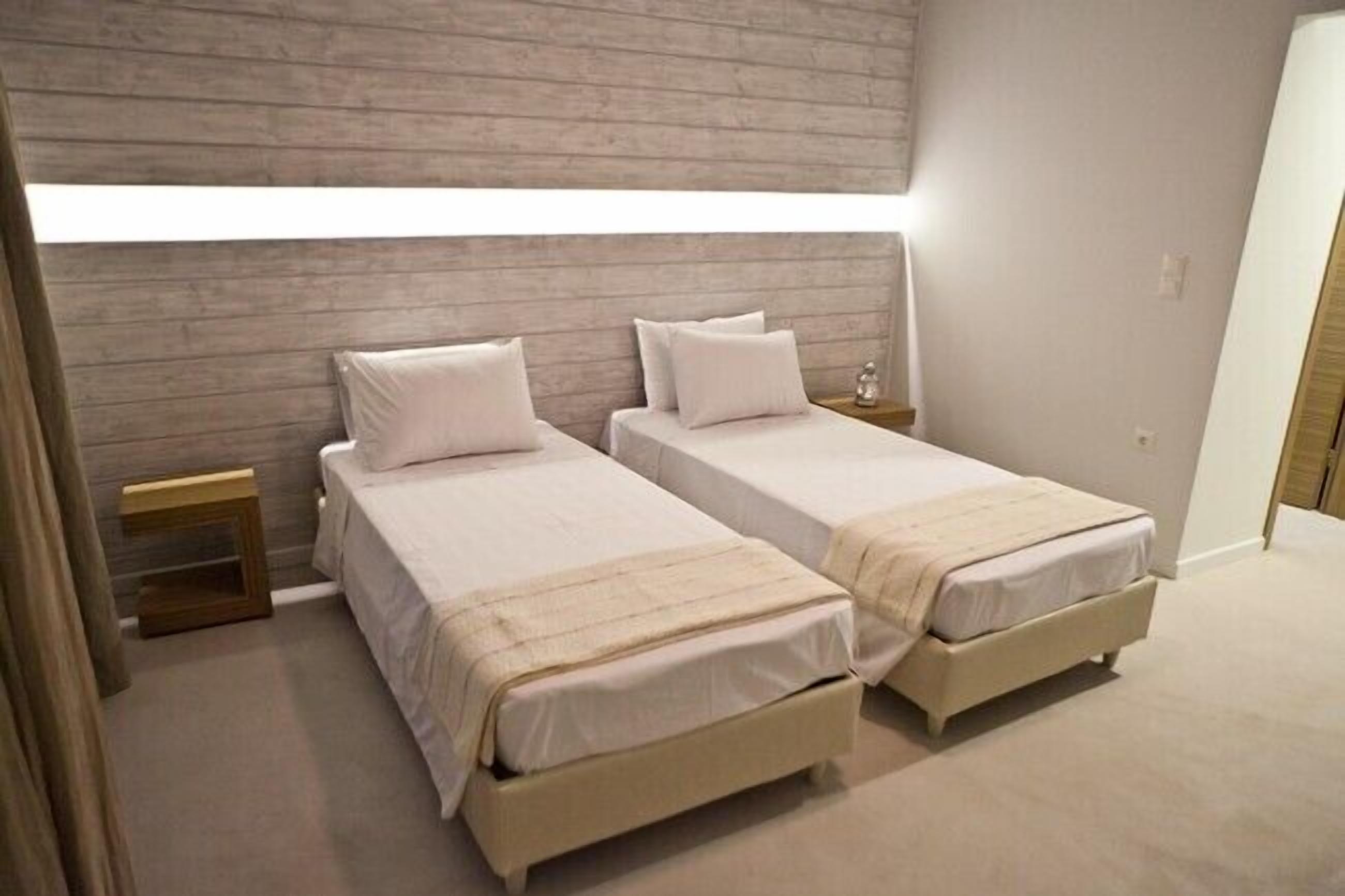 A bedroom with two beds, a wooden headboard, bedside tables, and a window.