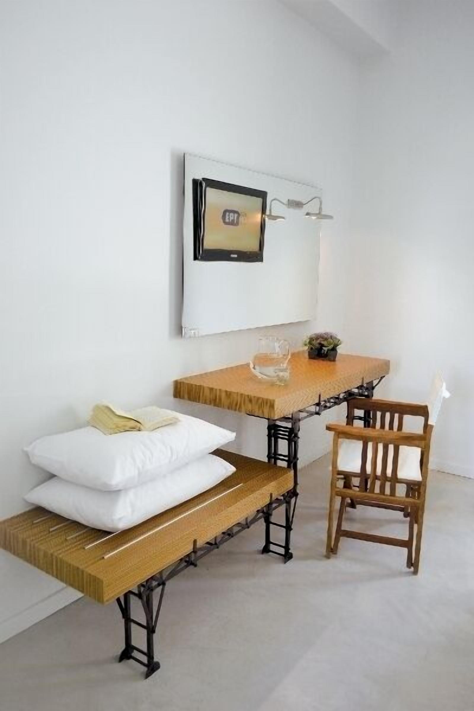 Una habitación pequeña y moderna con un banco de madera, una sola silla y un estante con un cuadro enmarcado.
