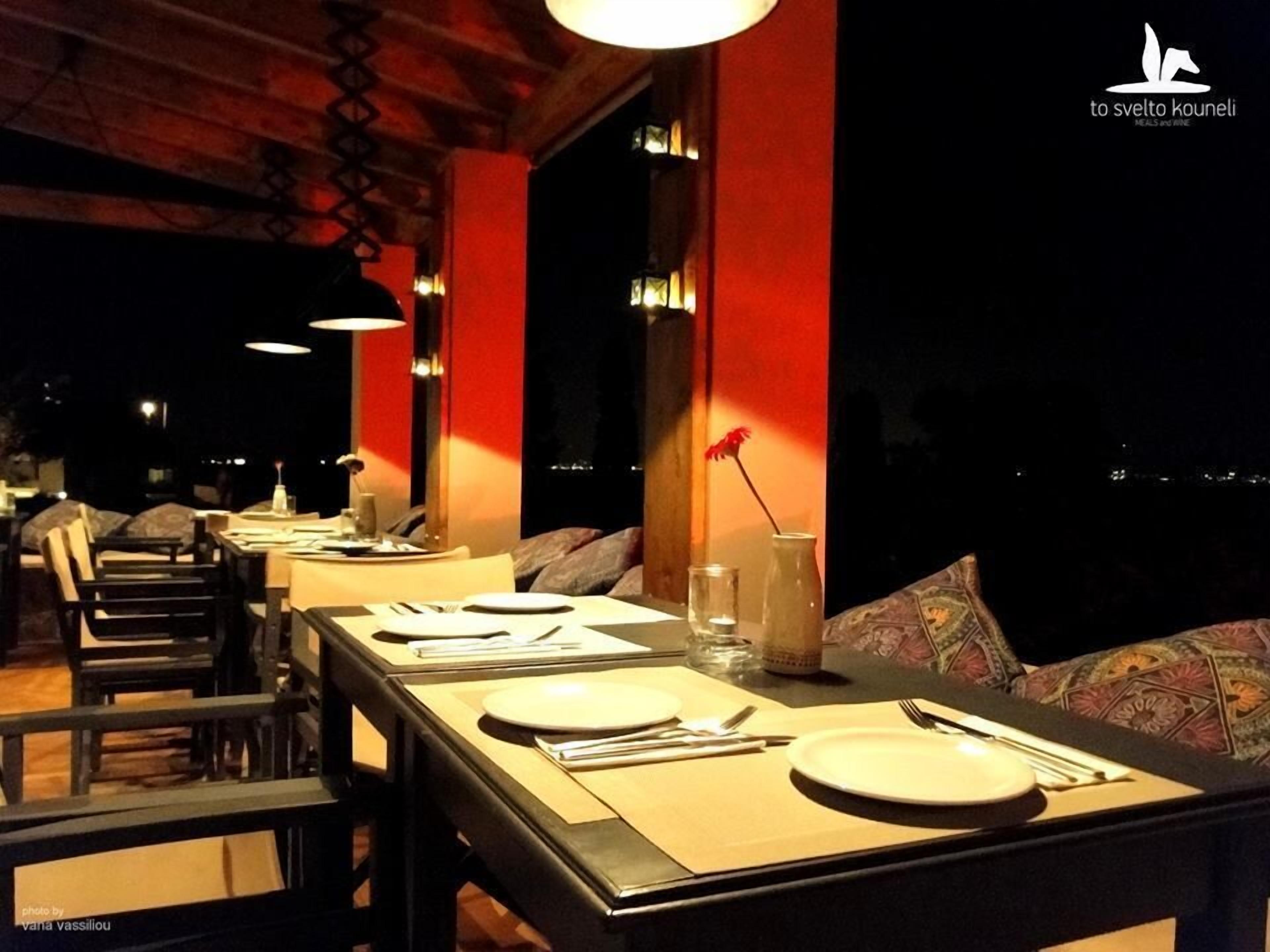 A restaurant with tables set for dining, featuring a modern design with red accents and a view of the city at night.