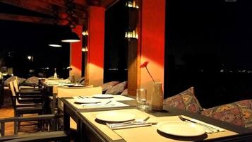 A restaurant with tables set for dining, featuring a modern design with red accents and a view of the city at night.