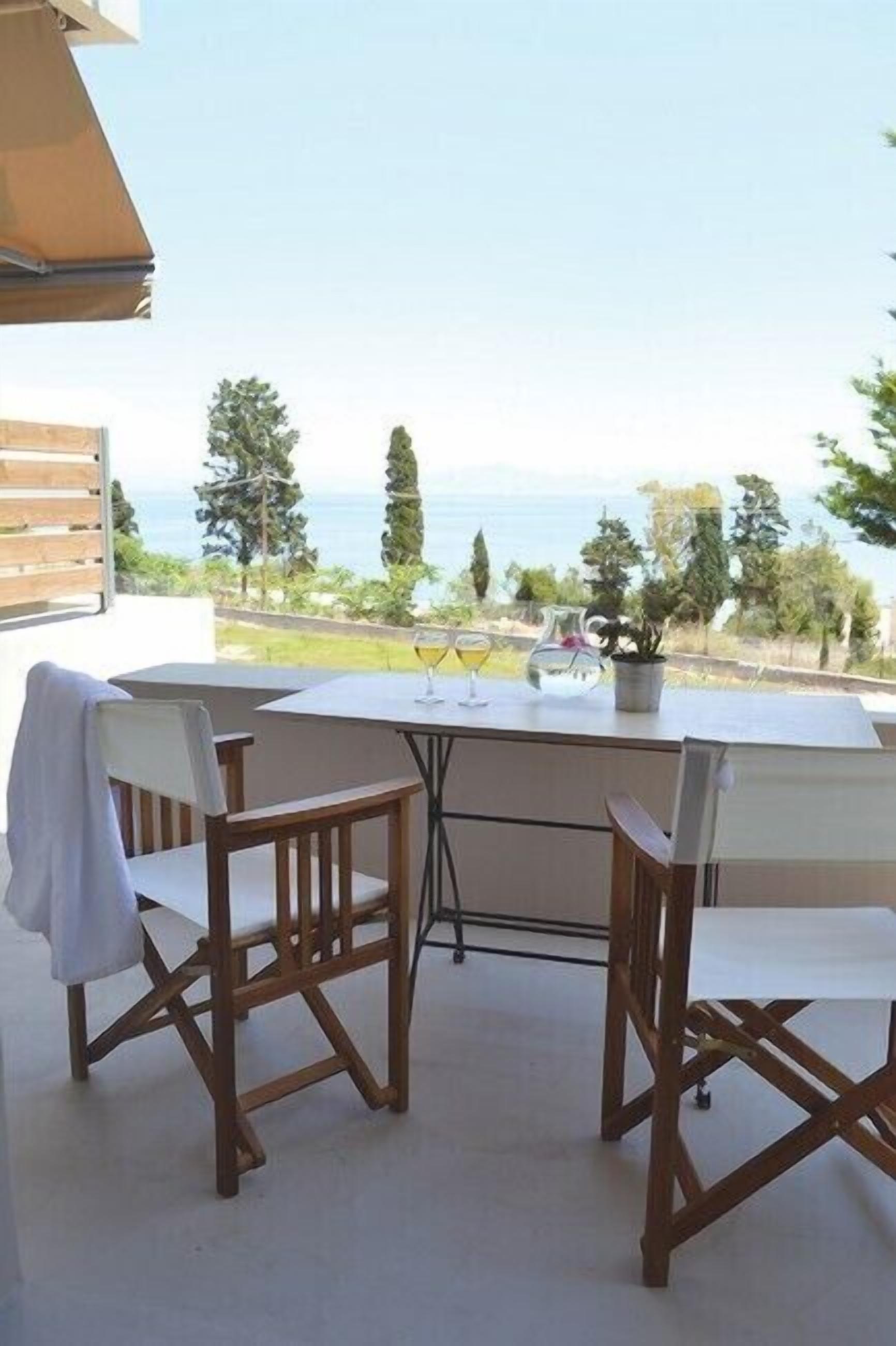 An outdoor patio with a table and chairs, a glass of wine, and a view of the sea.