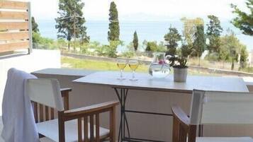 An outdoor patio with a table and chairs, a glass of wine, and a view of the sea.