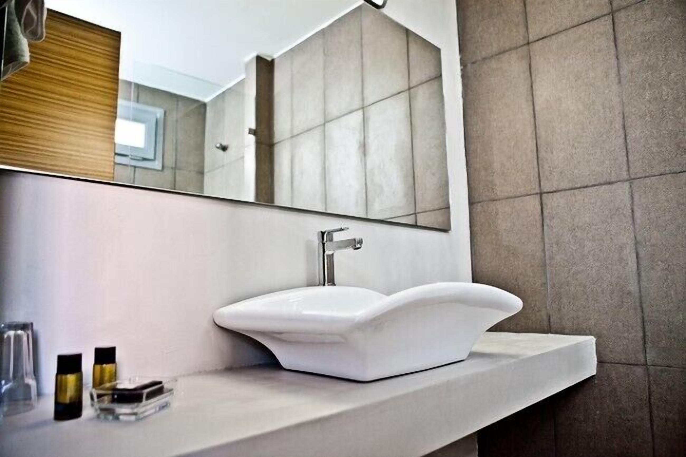 Un baño moderno con un lavamanos pedestal blanco, un espejo grande y una pared revestida de azulejos.