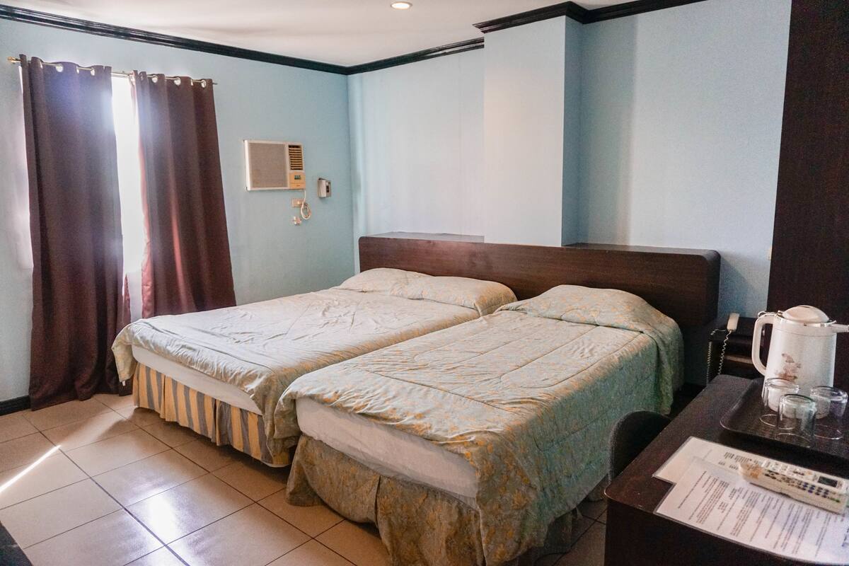 A hotel room with two beds, a desk with a telephone, a coffee maker, and a window with curtains.