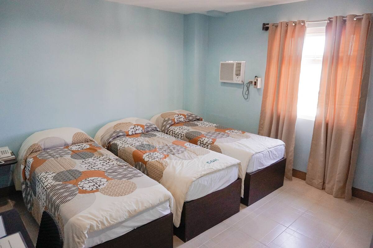 A room with two beds, a nightstand, a wall-mounted air conditioner, and a window with curtains.