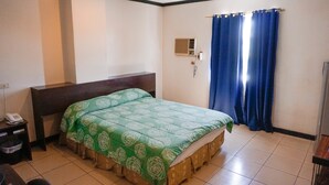 A hotel room with a single bed, a bedside table with a phone, and a wall-mounted air conditioning unit. - Crowne Garden Hotel (Cebu City)