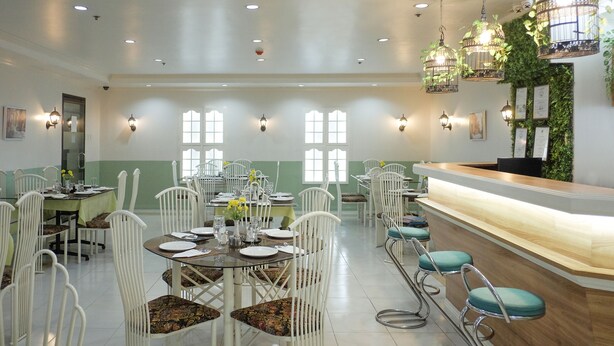 A spacious dining area with white chairs and tables, a bar with a wooden counter, and decorative wall lights. - Crowne Garden Hotel (Cebu City)
