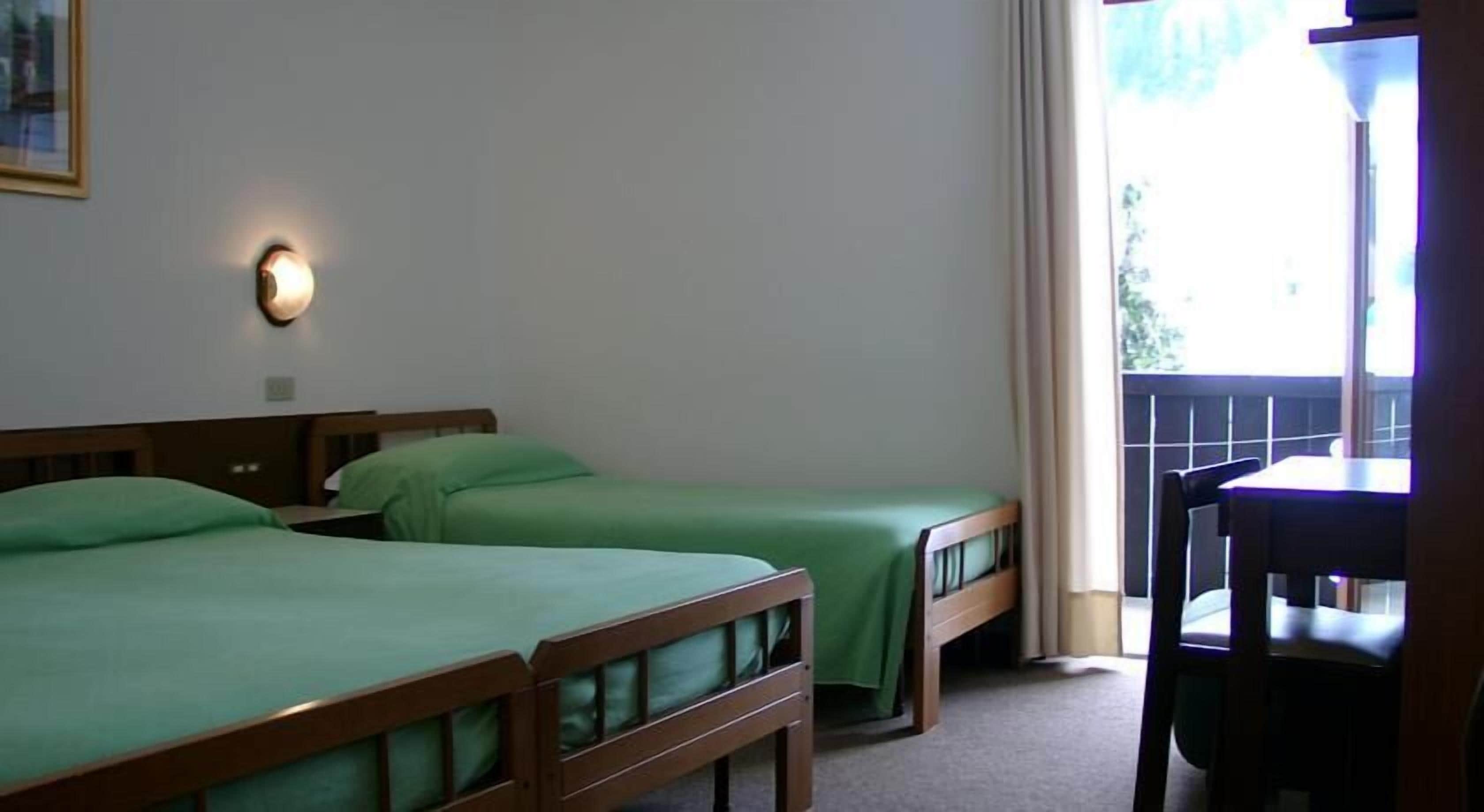 Ein Zimmer mit zwei Einzelbetten, einem Holzkopfende, einem kleinen Tisch und einem Fenster mit Vorhängen.