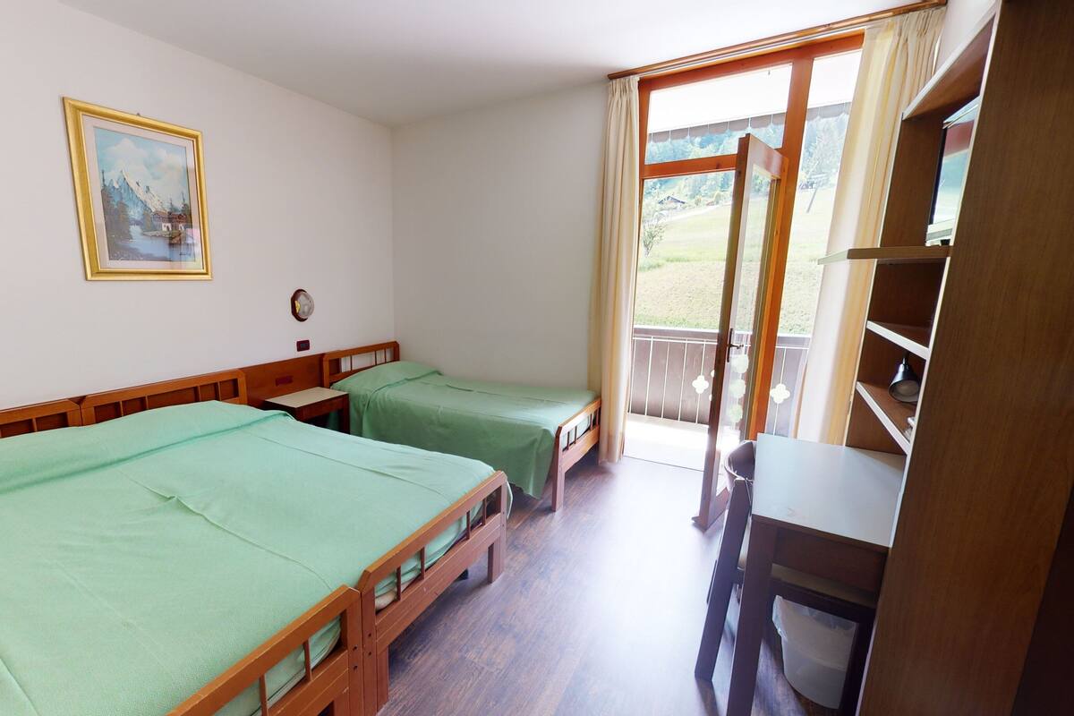 A room with two single beds, a wooden desk, a chair, a small table, a clock, and a framed picture on the wall.