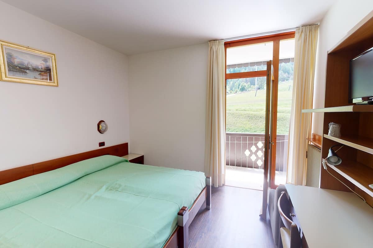 A hotel room with a bed, a desk with a chair, a television, and a window with curtains.