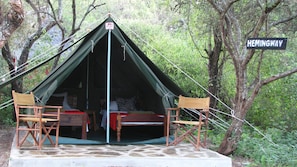 A tent with two wooden chairs and a table, surrounded by trees and a 'Hemingway' sign. - Maasai Simba Camp (Amboseli)