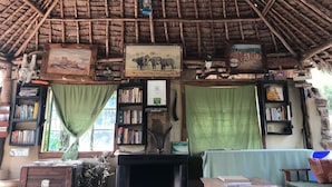 A rustic interior with a thatched roof, bookshelves, a fireplace, and a green curtain. - Maasai Simba Camp (Amboseli)