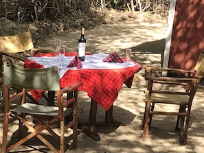 An outdoor dining area with a table covered in a red checkered tablecloth, surrounded by wooden chairs. - Maasai Simba Camp (Amboseli)