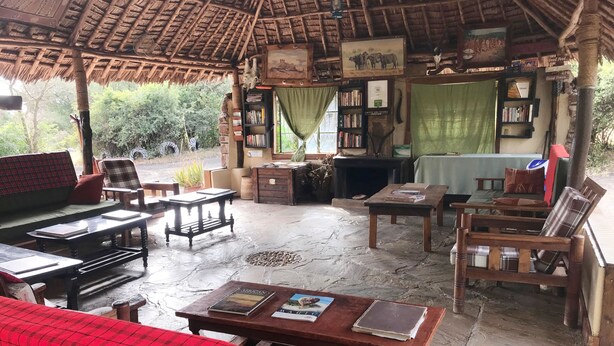 A rustic outdoor seating area with a thatched roof, wooden furniture, and a fireplace. - Maasai Simba Camp (Amboseli)