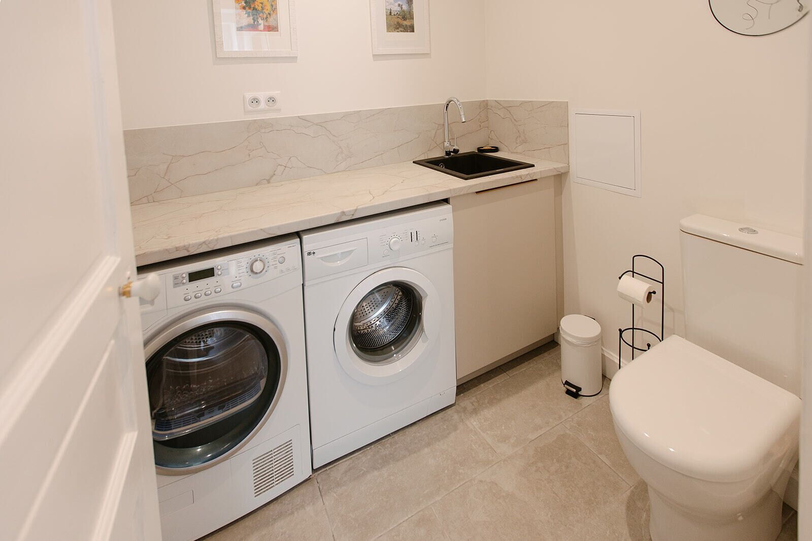 A compact laundry room with a washing machine, dryer, sink, and toilet.