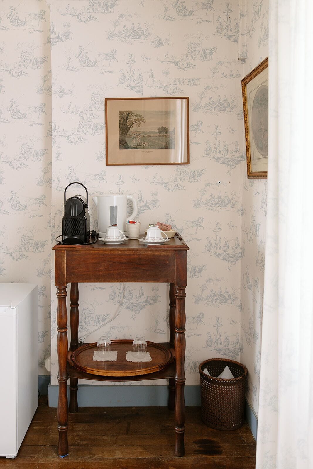 A corner room with a wooden table, a framed picture on the wall, and a white appliance in the corner.