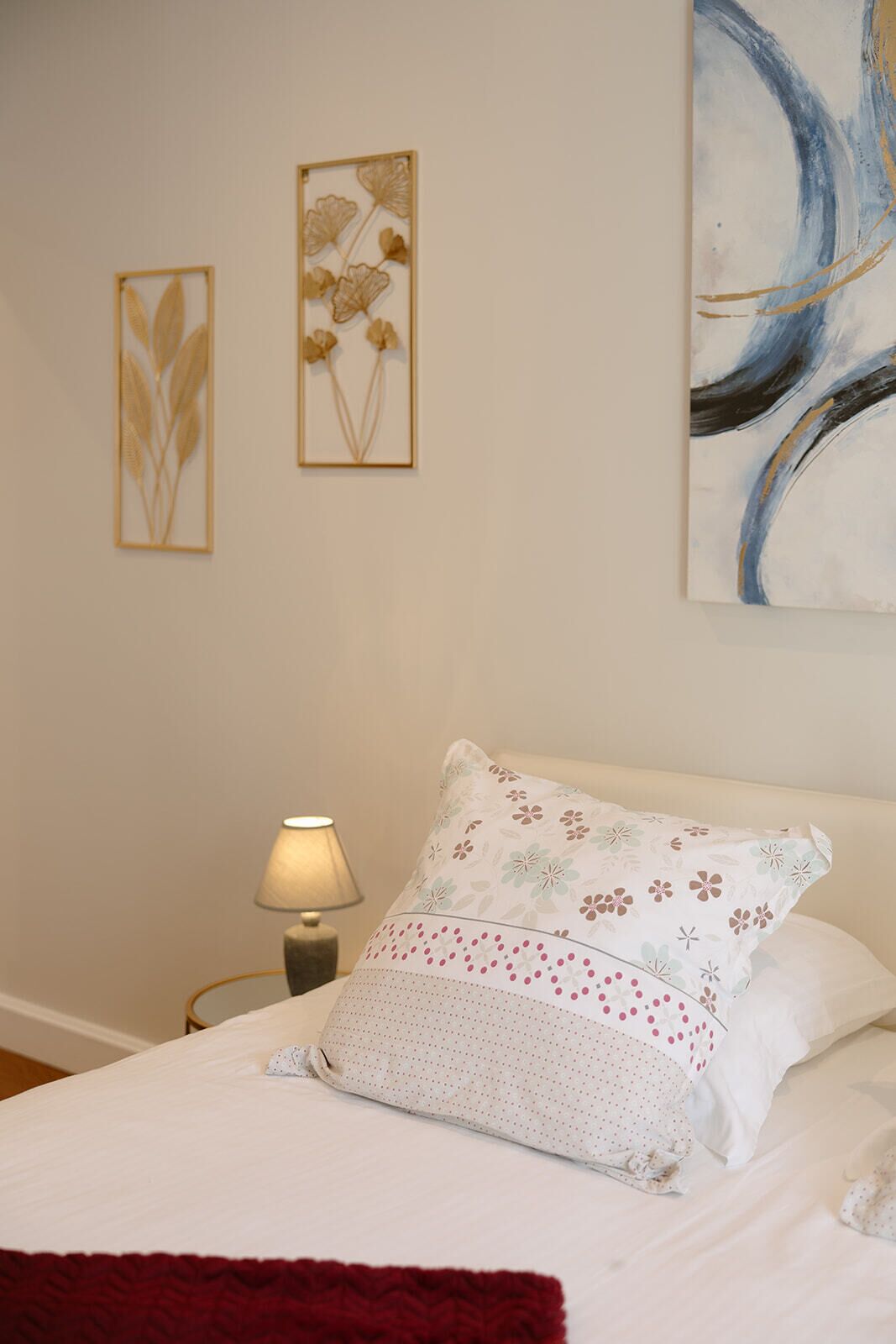 A bedroom with a bed, a nightstand with a lamp, and two framed artworks on the wall.
