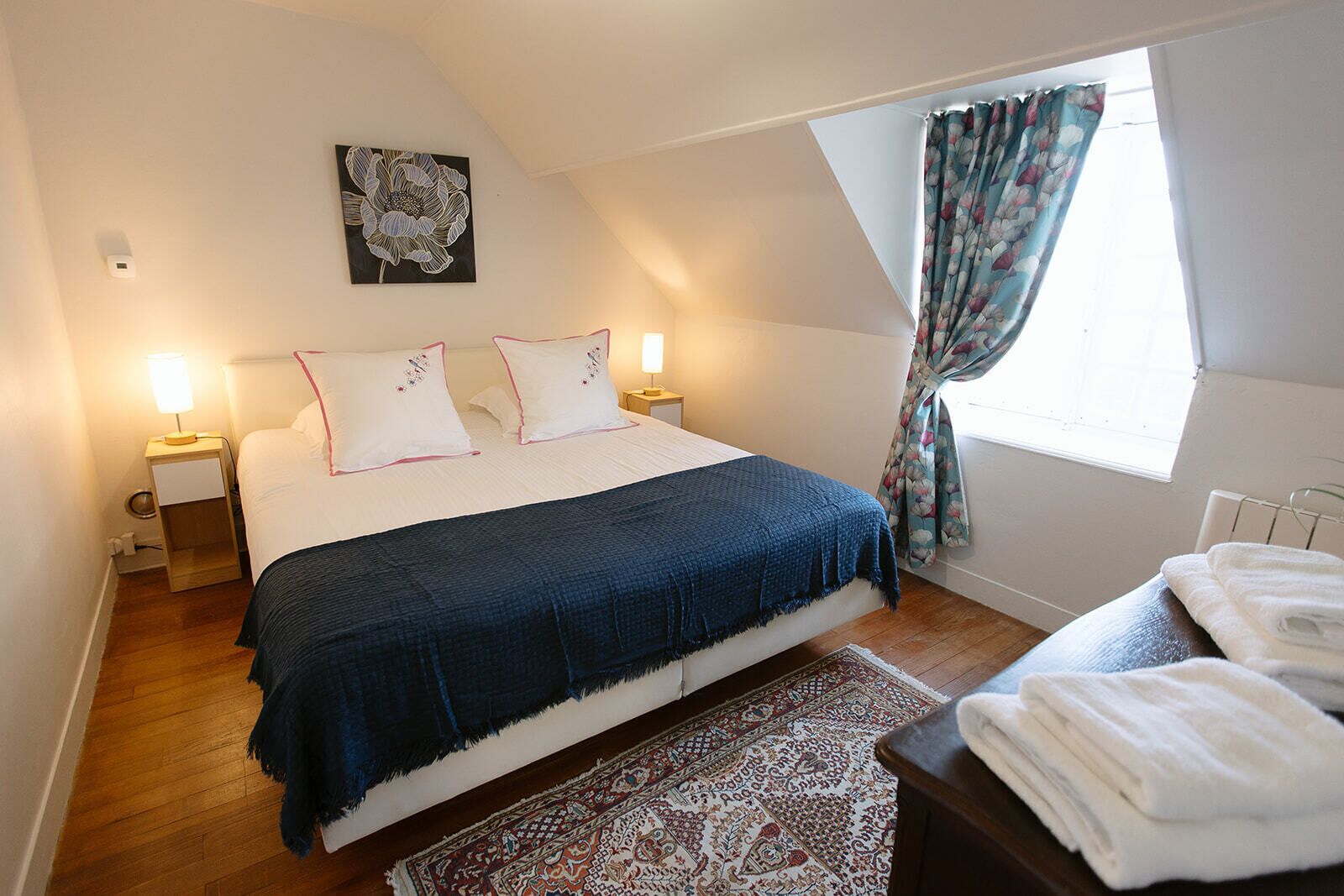 Ein Schlafzimmer mit Bett, Nachttischlampen, einem Fenster mit Vorhängen, einer Heizung und einem Teppich.